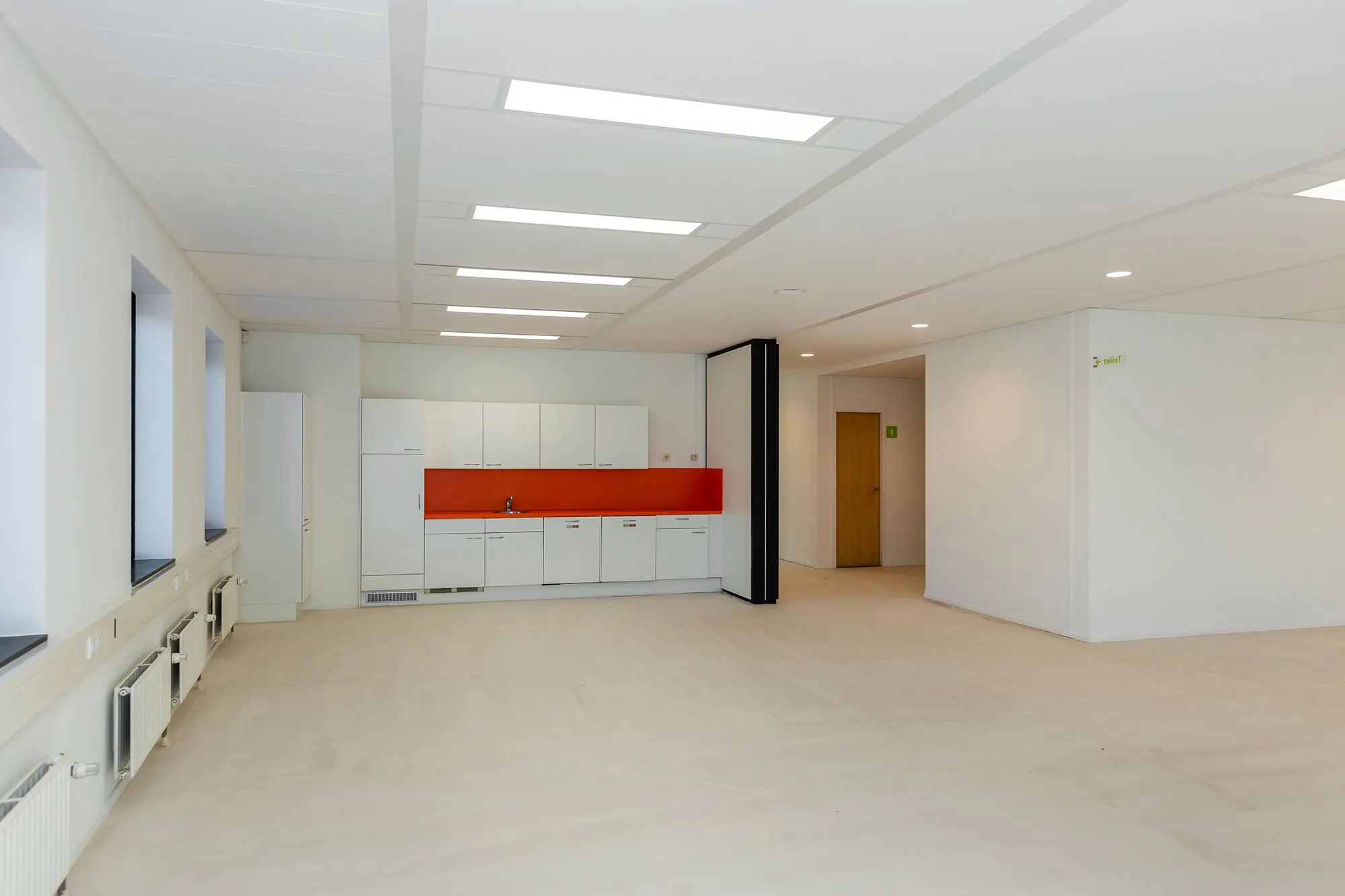 Moderne, lege kantoorruimte aan de Boris Pasternaklaan met een witte kitchenette en feloranje achterwand.